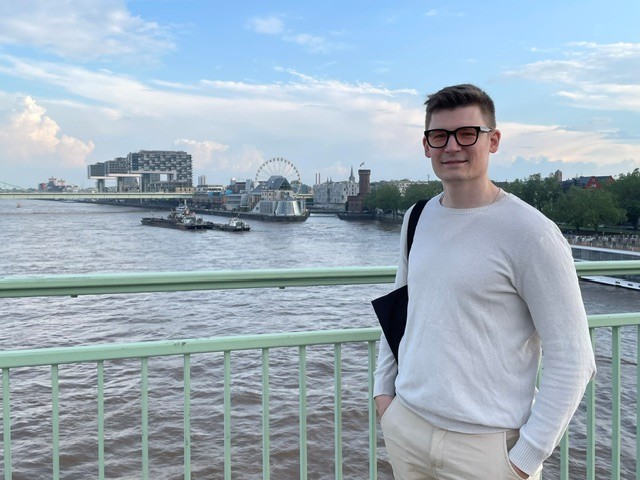 This is an image of the author in Cologne, Germany, staying on the Deutzer Bridge with Kranhäuser im Rheinauhafen in the background.